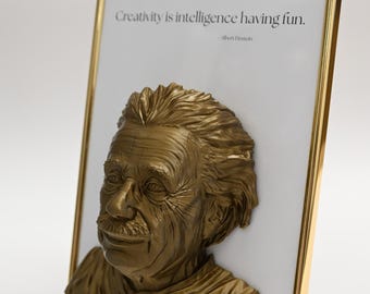 May include: A gold-colored framed picture with a 3D bust of Albert Einstein. The quote "Creativity is intelligence having fun. - Albert Einstein" is printed on the white background.