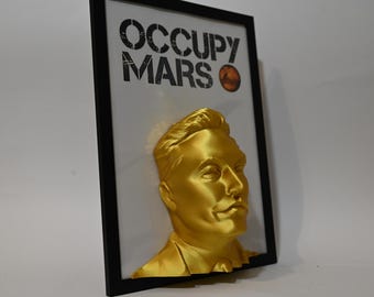 May include: A gold-colored 3D bust of a man's head in a black frame. The frame has a white background with the text "Occupy Mars" in black.
