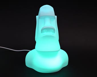 May include: A white ceramic lamp shaped like a Moai statue with a teal blue light emanating from the base.