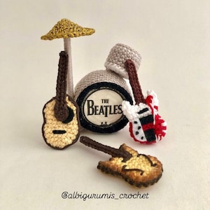 May include: Crocheted Beatles themed music set with a drum, two guitars, and a microphone stand. The drum has the words "The Beatles" printed on it.