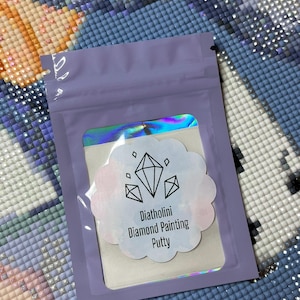 Könnte beinhalten: Eine kleine, wiederverschließbare lila Tasche mit einem transparenten Fenster, das einen weißen Aufkleber mit einem rosa-blauen Aquarellhintergrund zeigt. Der Aufkleber hat drei Diamantenformen und den Text "Diatholini Diamond Painting Putty".