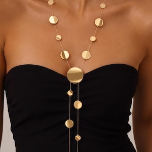 May include: A gold-toned Y-shaped necklace featuring a series of flat, circular discs of varying sizes suspended along thin, delicate chains. The design includes a larger central disc from which two separate chains descend, each adorned with smaller circular elements.