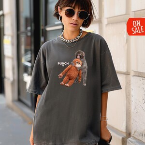 May include: Dark gray oversized t-shirt featuring a graphic of two monkeys. One is brown and the other is gray. The word "PUNCH" is printed on the shirt. The shirt has short sleeves and a relaxed fit.