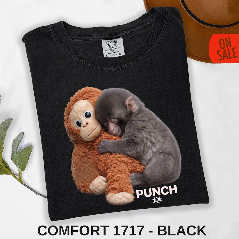 Baby macaque monkey sleeping while hugging a plush monkey toy printed on black t-shirt