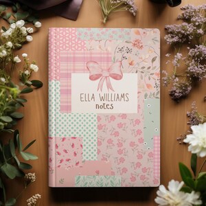 May include: A notebook with a patchwork design in shades of pink, mint, and white. The cover features a bow and the text "ELLA WILLIAMS notes". The notebook is surrounded by flowers and a cup of coffee.