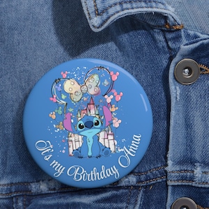 May include: A round, blue button featuring a cartoon character with large ears and a castle. The button has the text "It's my Birthday Anna" in a cursive font, with colorful accents and a bow design.