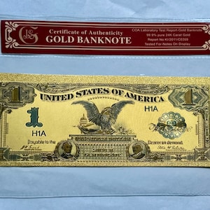 May include: A gold-plated $1 US banknote with a certificate of authenticity. The banknote features an eagle with outstretched wings, the words "United States of America", and the number "1" in the corners. The certificate of authenticity states that the banknote is 99.9% pure 24K carat gold.