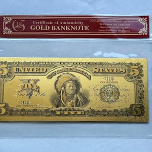 May include: A gold-colored five dollar bill with a portrait of an indigenous person in a feathered headdress. The bill is labeled "United States of America" and "Five Dollars." It is encased in a clear plastic sleeve with a certificate of authenticity.
