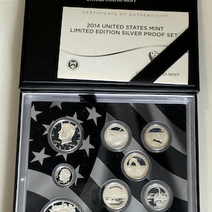 Puede incluir: Un set de monedas 2014 United States Mint Limited Edition Silver Proof Set en una caja negra. El conjunto incluye un certificado de autenticidad y ocho monedas de plata con varios diseños, incluyendo un medio dólar Kennedy y una moneda American Eagle.