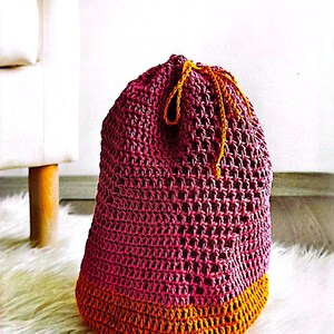 Puede incluir: Una bolsa de almacenamiento de crochet rosa y naranja con cierre de cordón. La bolsa está sentada sobre una superficie blanca y esponjosa.