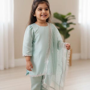 May include: A light mint green three-piece outfit consisting of a long-sleeved tunic with scalloped lace trim, matching straight-leg trousers with horizontal white stripes at the cuffs, and a sheer, polka-dot patterned dupatta with fringed edges.