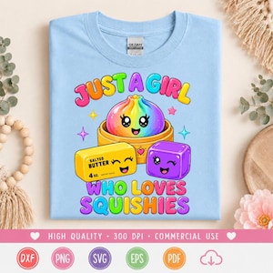 May include: A light blue t-shirt featuring a colorful graphic of a rainbow dumpling in a bamboo steamer, a yellow stick of salted butter, and a purple cube. The text reads JUST A GIRL WHO LOVES SQUISHIES. The shirt has a Gildan brand neck label.