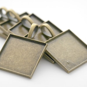 May include: A stack of six antique brass square pendant trays with a beveled edge and a loop for hanging.