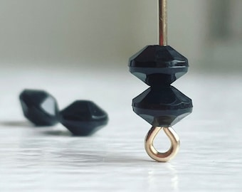 Pode incluir: Duas contas facetadas pretas enfiadas em um fio de ouro com um anel de salto dourado na ponta.