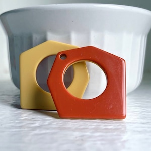 Può includere: Due portachiavi di forma geometrica, uno è giallo chiaro e l'altro è rosso arancione.