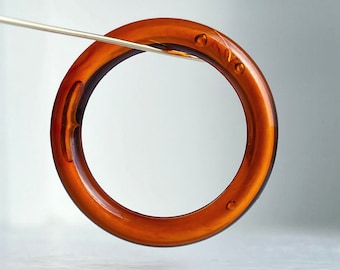Op de afbeelding: Een bruine plastic ring met een gladde, glanzende afwerking. De ring is ongeveer 5 cm in diameter en heeft een kleine, ronde opening aan de ene kant.