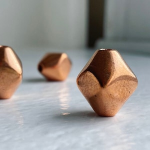 May include: Three copper-coloured, faceted, geometric beads. The beads are shaped like a diamond with a pointed top and bottom.