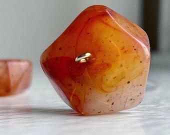 Può includere: Primo piano di un tallone di cornalina con un anello di metallo dorato. Il tallone è di colore arancione intenso con striature marroni e bianche.