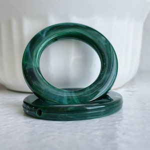 May include: Two green and white marbled plastic curtain rings. The rings are stacked on top of each other.