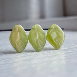 Op de afbeelding: Drie groene, bladvormige kralen met een gesneden ontwerp. De kralen zijn gemaakt van een doorschijnend materiaal en hebben een lichtgroene kleur.
