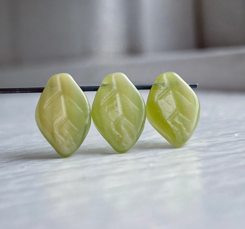 Op de afbeelding: Drie groene, bladvormige kralen met een gesneden ontwerp. De kralen zijn gemaakt van een doorschijnend materiaal en hebben een lichtgroene kleur.