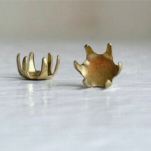 May include: Two gold-toned metal settings for a cabochon stone. The settings have a scalloped edge and a flat base.