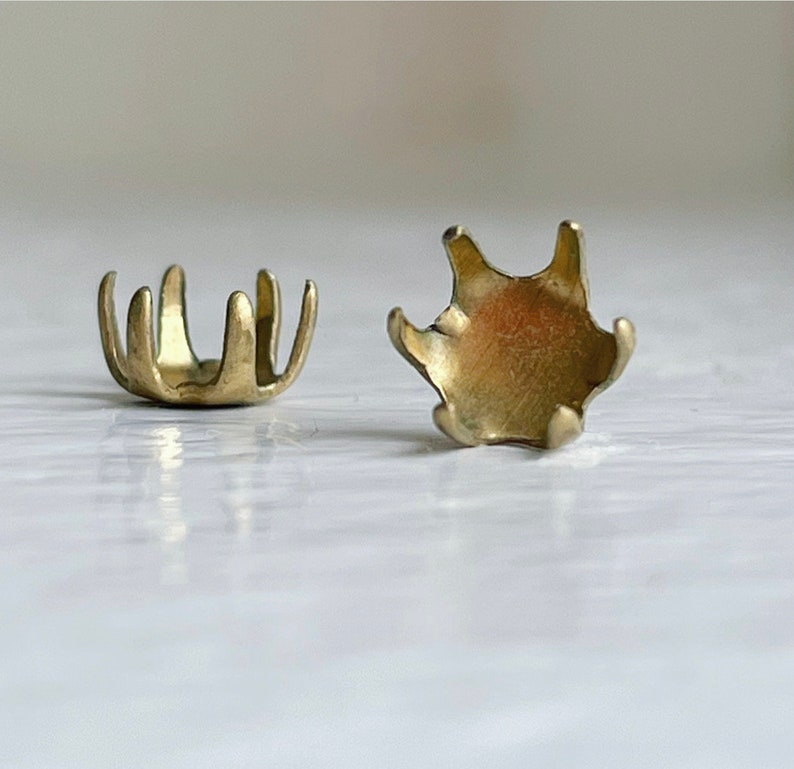May include: Two gold-toned metal settings for a cabochon stone. The settings have a scalloped edge and a flat base.