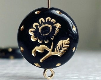 May include: Black and gold round bead with a floral design. The bead has a gold loop on the bottom.