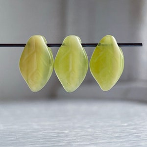Op de afbeelding: Drie lichtgroene glazen kralen in de vorm van een blad, geregen aan een zwarte draad.