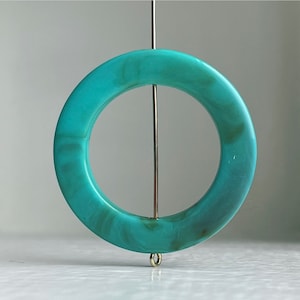 Op de afbeelding: Een tealblauwe cirkelhanger met een marmer effect. De hanger hangt aan een dunne gouden ketting.