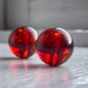 May include: Two round, translucent, amber-colored beads. The beads have a glossy finish and reflect light, creating highlights and shadows. The beads are likely made of glass or resin and are suitable for jewelry making.