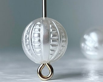May include: A white pearl bead with a textured surface and a gold loop attached. The bead is on a white background.