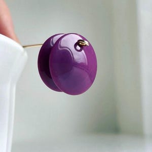 May include: A pair of purple, round, shiny earrings with a gold hook.