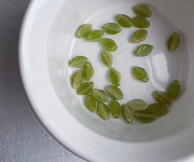 Op de afbeelding: Een witte kom gevuld met groene, blaadjesvormige snoepjes. De snoepjes zijn in een willekeurig patroon gerangschikt.