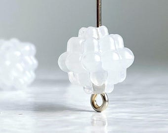 May include: White opaque glass bead with a cluster of small round beads, attached to a silver loop.
