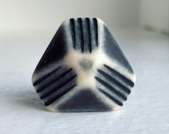 Pode incluir: Um botão de cerâmica geométrico branco e preto com um design de estrela. O botão tem uma superfície texturizada e tem a forma de uma pirâmide.