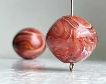 Può includere: Due perline di vetro rosa e bianco con effetto vortice. La perlina a sinistra è sfocata e la perlina a destra è a fuoco e appesa a un filo d'argento.
