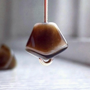 May include: A brown and white glass bead with a unique shape, hanging from a silver wire.