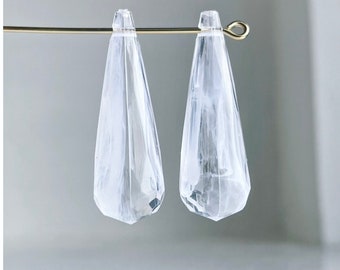 May include: Two clear glass teardrop-shaped beads with a white marbled pattern hanging from a gold wire.