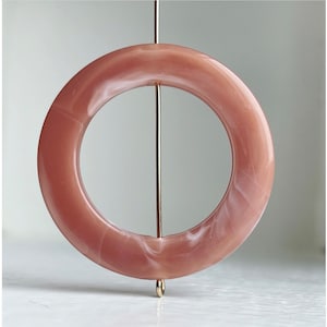 May include: A pink and white marbled ring with a gold metal pin. The ring is a circle with a hole in the center.