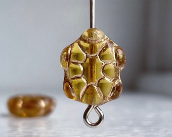 May include: A gold-toned glass bead with a textured, geometric design. The bead is attached to a silver-toned wire loop.