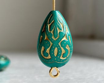 May include: A teardrop-shaped bead in a vibrant turquoise color featuring intricate gold-colored filigree patterns and small dots. The bead is suspended on a thin gold-colored metal pin and includes a small gold-colored metal loop at the bottom.
