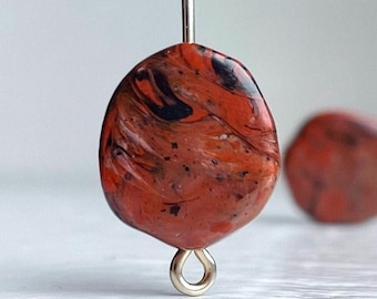Può includere: Un paio di orecchini marmorei arancioni e neri con un gancio d'argento. Gli orecchini sono realizzati in argilla polimerica e hanno un motivo unico a spirale.