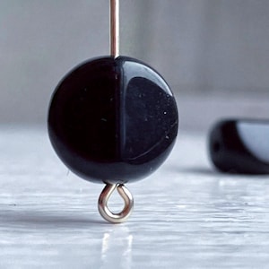 May include: A black round bead with a silver loop attached. The bead is smooth and shiny.