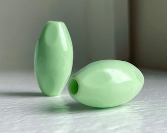 Pode incluir: Duas contas de plástico ovais de cor verde claro. As contas são lisas e brilhantes.