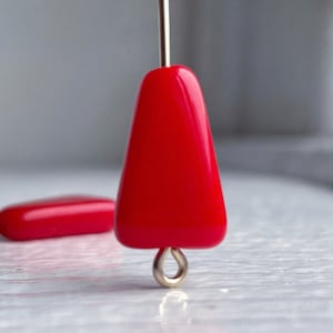 May include: A bright red glass bead with a triangular shape and a gold metal loop at the bottom.