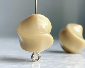 Pode incluir: Um par de brincos de cerâmica bege com forma retorcida e orgânica. Os brincos têm um laço prateado para pendurar.