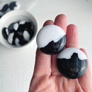 May include: Two round, black and white, decorative, resin, paperweights. The paperweights are half black and half white, with a wavy line separating the two colors.