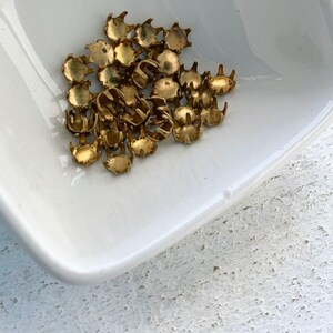 May include: A pile of gold-colored metal claw-shaped studs in a white ceramic dish.