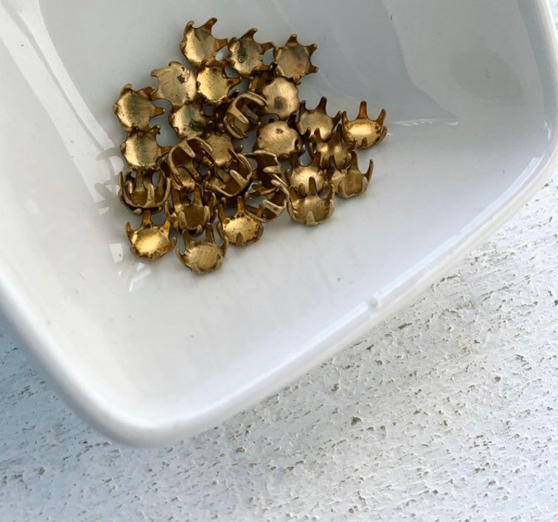 May include: A pile of gold-colored metal claw-shaped studs in a white ceramic dish.